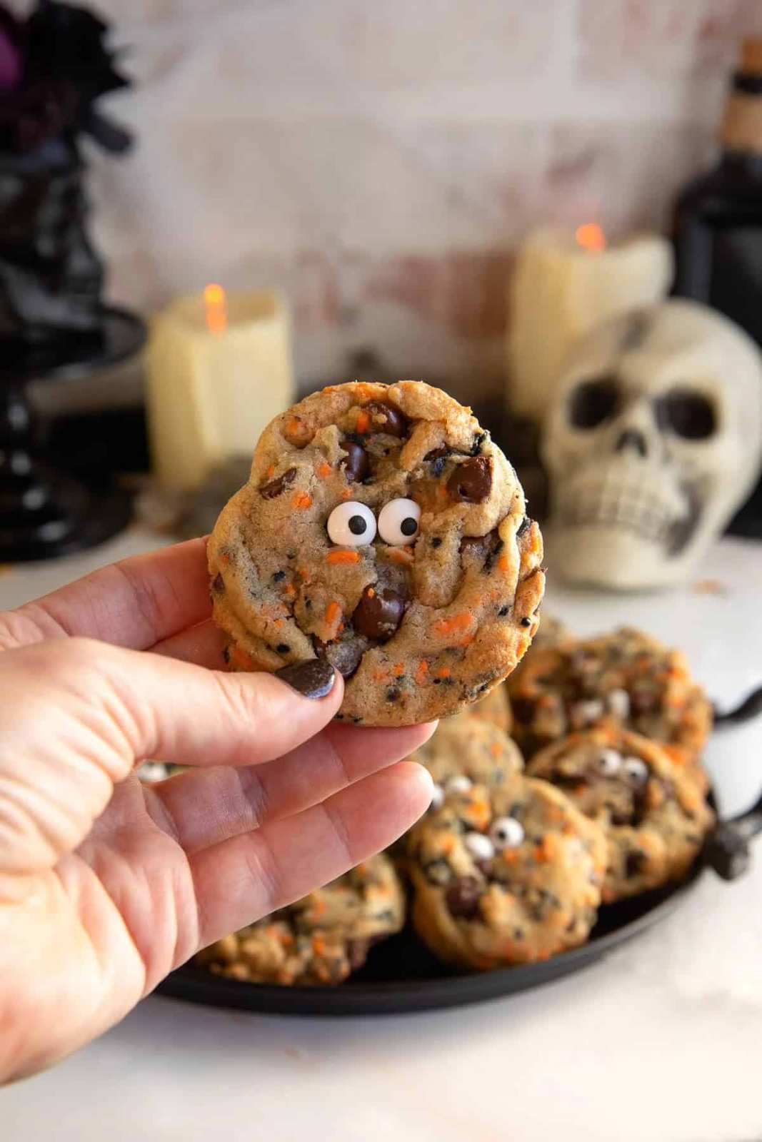 Soft chocolate chip cookies with orange icing drips and black candy eyes on a festive plate